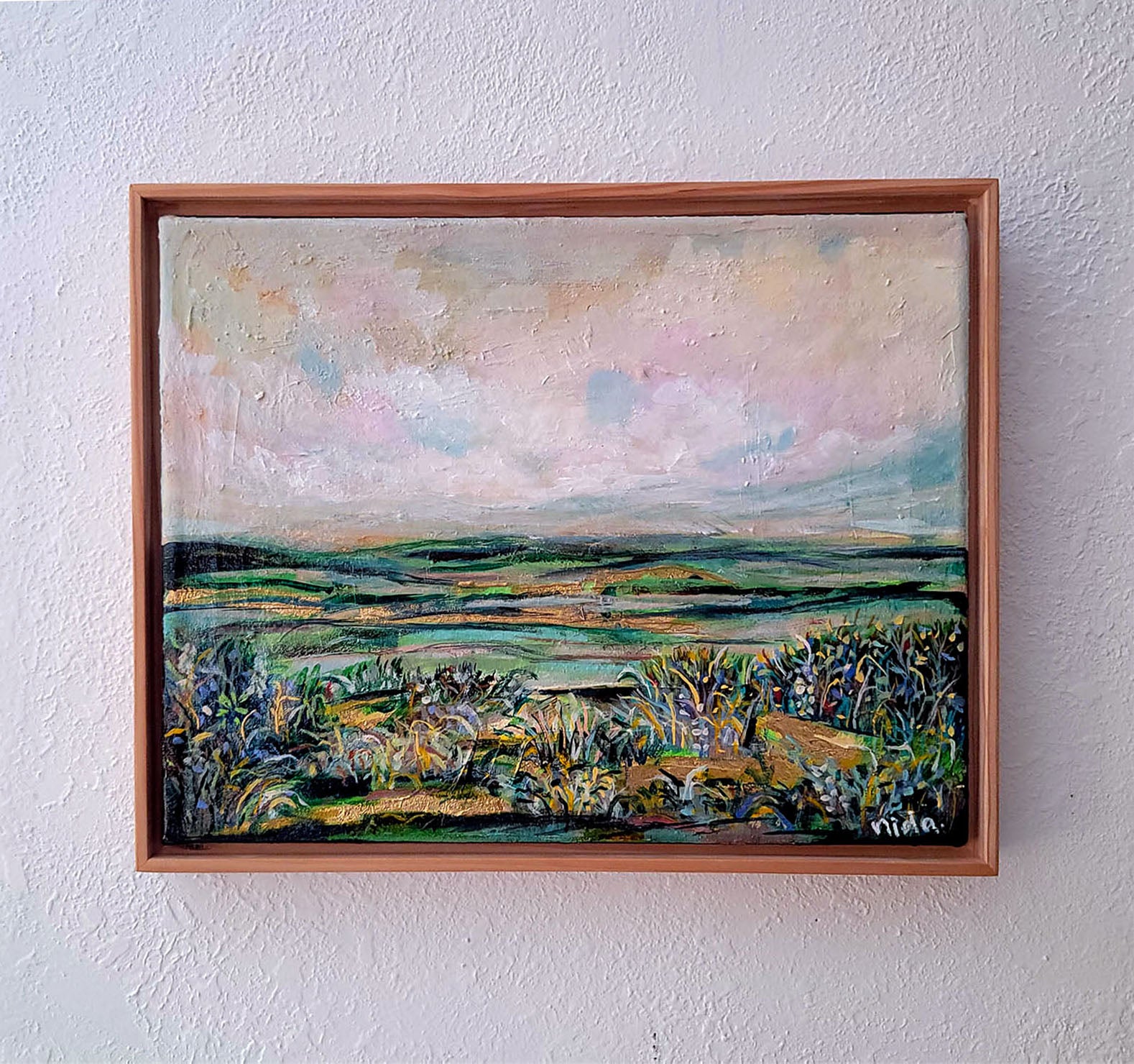 Framed painting of a landscape with a wooden frame on a white wall